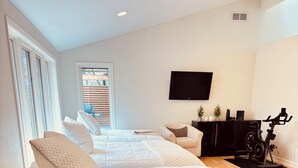 Un dormitorio moderno con una cama grande, televisión, escritorio y bicicleta estática.