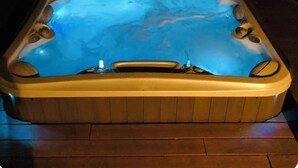 Un jacuzzi con interior de madera y superficie de agua iluminada en azul.