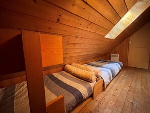 Ein kleines, gemütliches Schlafzimmer im Dachgeschoss mit Holzwänden und geneigten Decken, mit zwei Betten mit gemusterten Bettbezügen und einem Nachttisch.