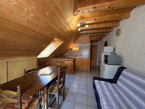 Ein gemütliches Schlafzimmer im Dachgeschoss mit Holzbalkendecke, einem Esstisch, einer Couch und einer Küchenzeile.