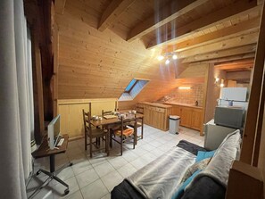 Ein gemütliches Dachzimmer mit Esstisch, Stühlen, einer Couch, einer kleinen Küchenzeile und einem Oberlicht.