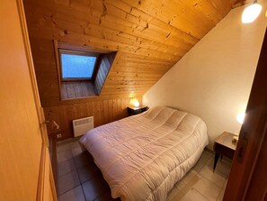 Ein Schlafzimmer mit schrägem Dach, einem Fenster, einem Bett, einem Nachttisch und einem Heizgerät.