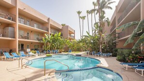 Ein Hotelpool mit blauen Liegestühlen, Palmen und einem mehrstöckigen Gebäude mit Balkonen.