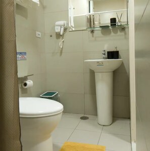 A bathroom with a toilet, a sink, a hairdryer, a trash bin, and a toilet paper roll. - Greenleaf fast Wifi Green Residence (Manila)