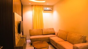 A modern living room with a sectional sofa, a wooden coffee table, a flat-screen TV, and an air conditioning unit.