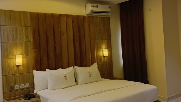 A modern hotel room with a large bed, wooden headboard, and built-in lighting.
