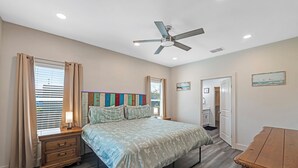 A bedroom with a bed, bedside table, nightstand, ceiling fan, and a door leading to another room. - 3 BD Family Home | Extd Stays | Pets Ok (Aransas Pass)