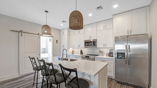 A modern kitchen with white cabinets, a stainless steel refrigerator, a large island with bar stools, and pendant lighting. - 3 BD Family Home | Extd Stays | Pets Ok (Aransas Pass)