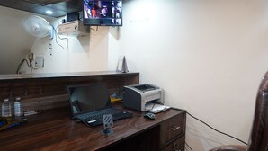 Un escritorio de madera con una computadora portátil, una impresora, un ventilador y un televisor montado en la pared.