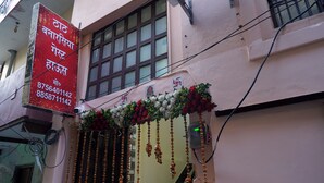 Fachada de edificio con letrero, ventana y adornos florales colgantes.