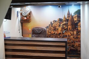 Een kamer met een houten bureau, een ventilator aan de muur en een groot poster van een historisch stadsgezicht.