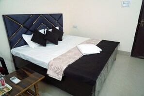 A neatly made bed with a patterned bedspread, a bedside table with a remote control, and a wall socket. - Thath Banarasiya (Varanasi)