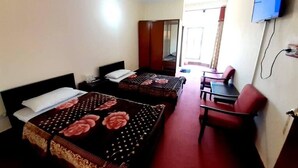 Une chambre d’hôtel avec deux lits, un bureau, une chaise, une télévision et un ventilateur de plafond.