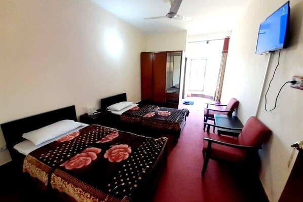A hotel room with two beds, a desk, a chair, a television, and a ceiling fan.