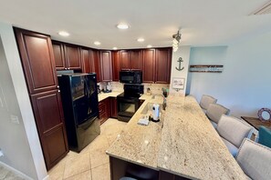 Eine Küche mit Holzausstattung, einer Granitarbeitsplatte, einem Kühlschrank, einer Mikrowelle und einem Spülbecken.
