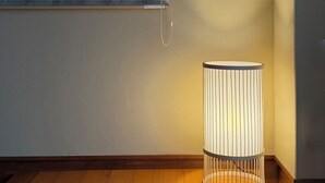 A corner room with a wooden floor, a wall-mounted light fixture, and a window with blinds. - Namiki Hills (Hiroshima)
