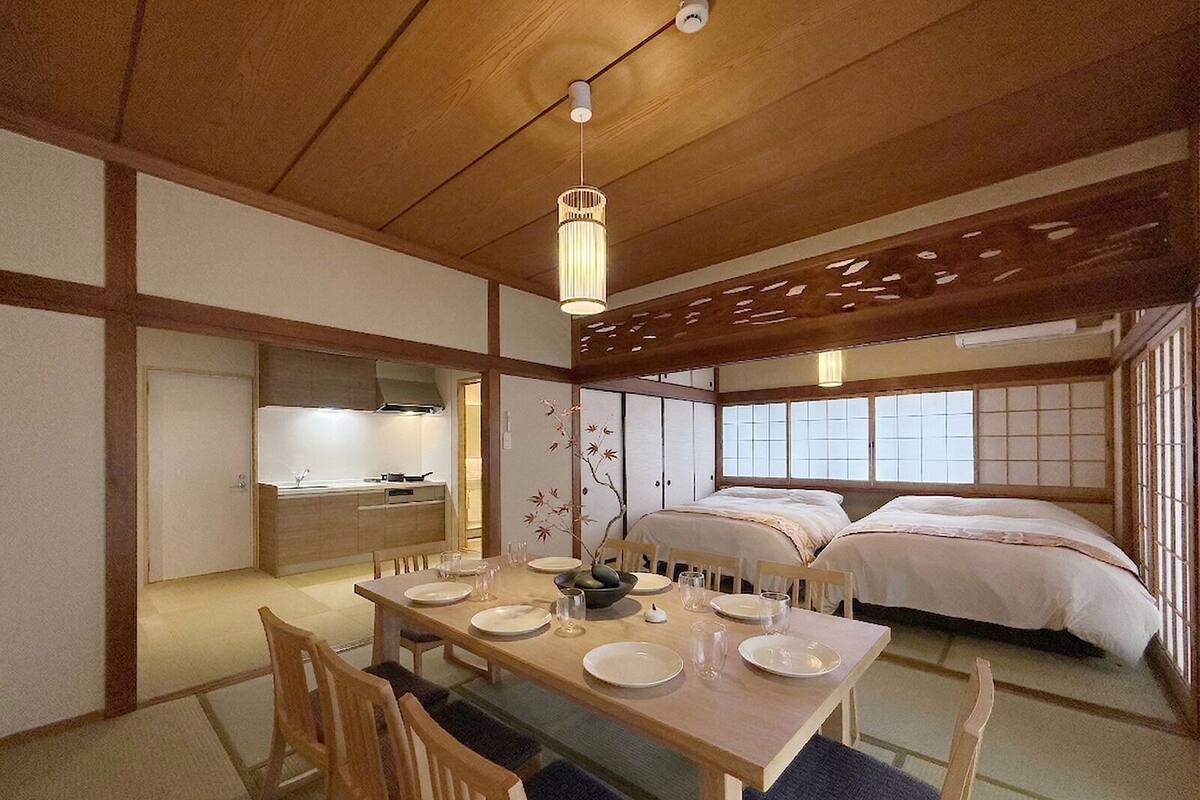 Una habitación tradicional japonesa con suelo de tatami, una mesa de madera para dos personas, una cama con colchones futón y una puerta corredera de shoji.