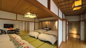 A traditional Japanese-style room with tatami flooring, two beds, a dining area with a table and chairs, and a television. - Namiki Hills (Hiroshima)