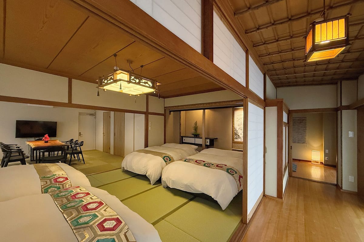 Perinteinen japanilaistyylinen huone, jossa on tatamimatto, kaksi sänkyä, ruokailutila pöydän ja tuolien kera sekä televisio.