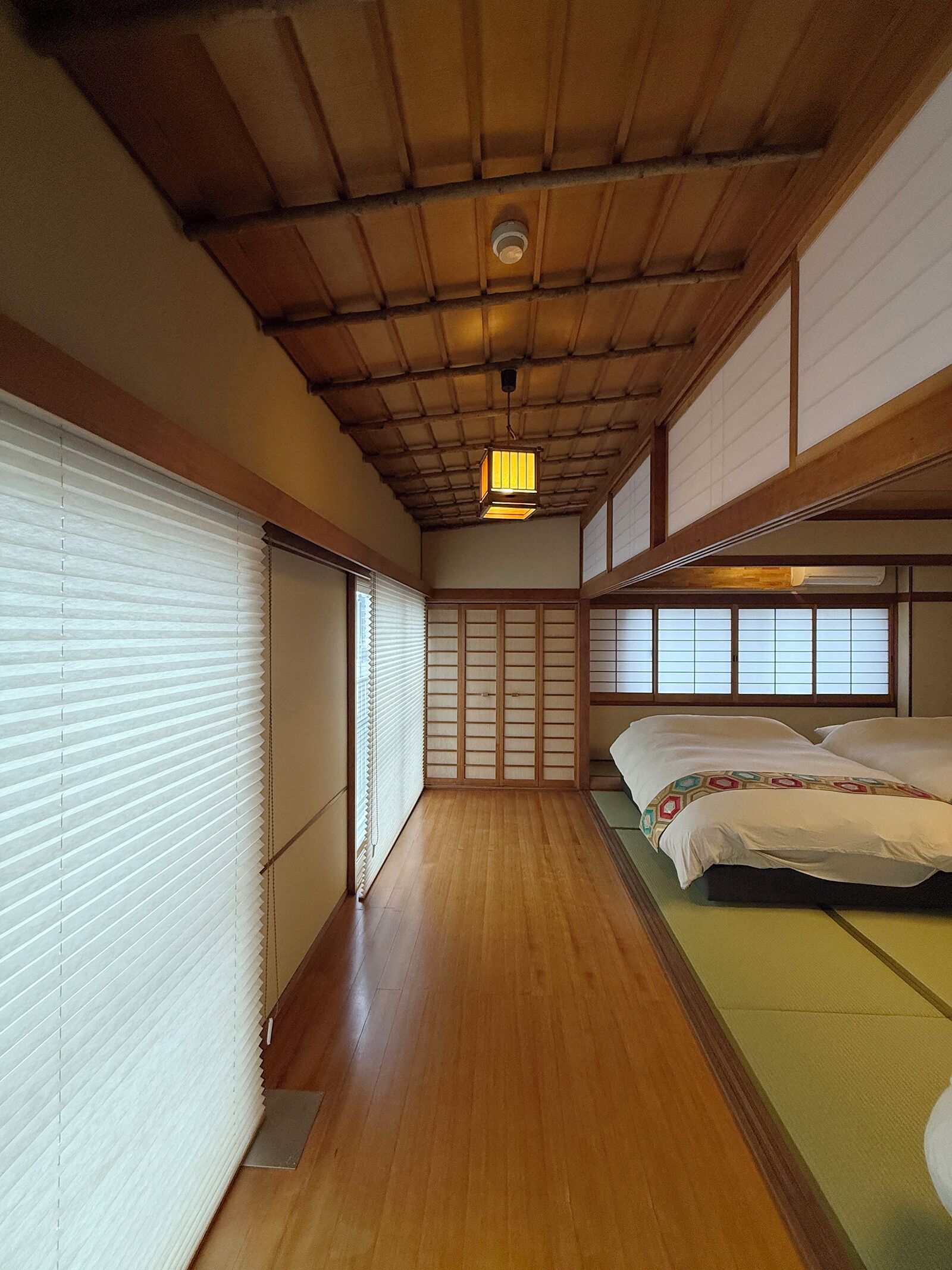 Et traditionelt japansk rum med tatamimåtter, en futon-madras, skydedøre og et loft med synlige træbjælker.