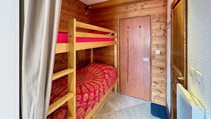 Een slaapkamer met een houten stapelbed, een deur en een radiator.