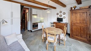 Een kleine keuken met witte kastjes, een houten eettafel met stoelen, en een grote houten kast.