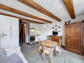Eine kleine Küche mit weißen Schränken, einem Holztisch mit Stühlen und einem großen Holzschrank.