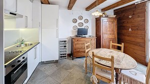 Een keuken met een fornuis, gootsteen en kasten, een houten eettafel met stoelen, en een houten wand.