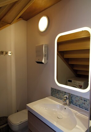 Ein Badezimmer mit weißem Waschbecken, einem Spiegel, einer Toilette und einem Händetrockner.