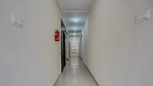 A corridor with white walls, a fire extinguisher, and a ceiling light. - Deluxe Venkat Inn (Bengaluru)