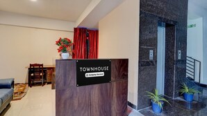A reception desk labeled 'TOWNHOUSE' with a 'Company-Serviced' sign, a red curtain, a potted plant, a blue sofa, and a tiled floor. - Deluxe Venkat Inn (Bengaluru)