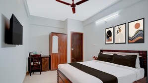 A bedroom with a bed, a wardrobe, a desk, a chair, a ceiling fan, and wall art. - Deluxe Venkat Inn (Bengaluru)