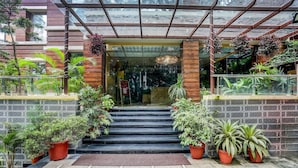 Entrada de un hotel con puerta de vidrio, escalones que conducen a ella y plantas en macetas a ambos lados.