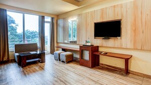 Una habitación de hotel moderna con piso de madera, un sofá, una mesita, un banco y un televisor montado en la pared.