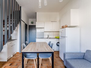 A compact kitchen with a dining table, chairs, a washing machine, and a sofa.