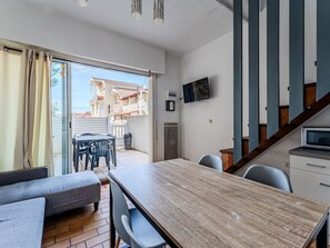 A room with a wooden dining table, grey sofa, and a TV mounted on the wall.