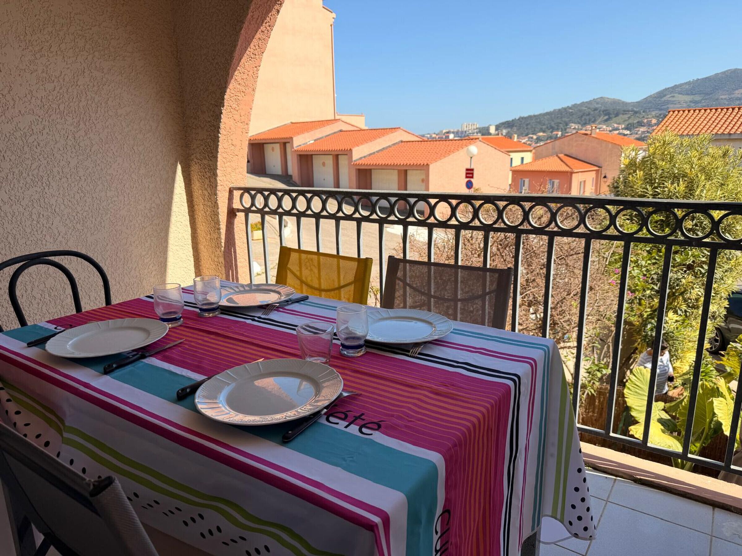 Un balcon avec une table dressée pour deux personnes, donnant sur un quartier résidentiel avec des maisons et des collines.