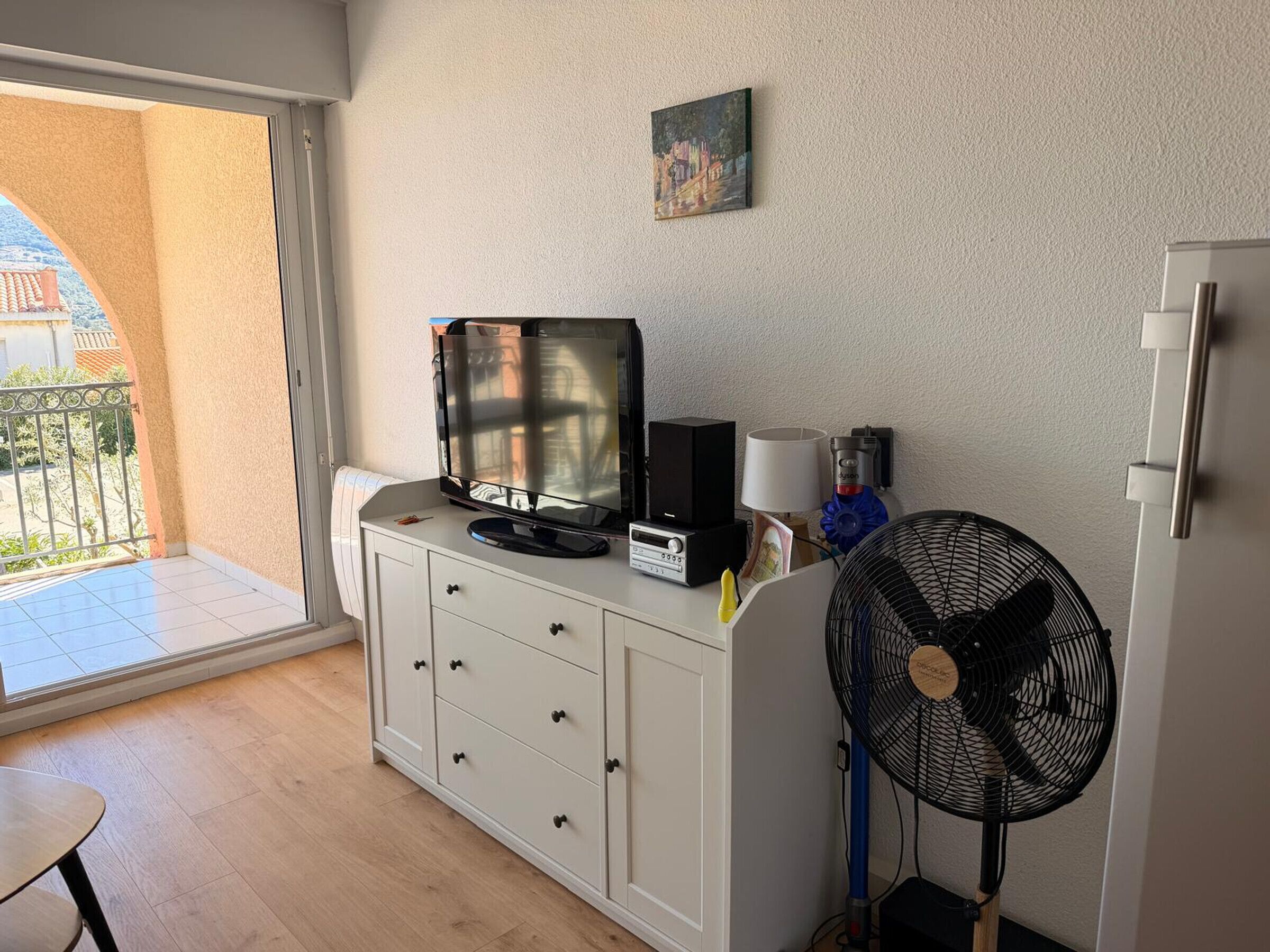 A room with a TV on a cabinet, a fan, and a small painting on the wall.