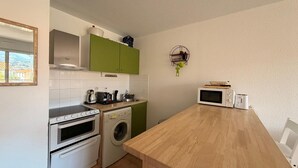 Ett kompakt kök med tvättmaskin, ugn, mikrovågsugn och ett träbord.