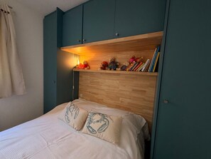A bedroom with a bed, a shelf with books and stuffed animals, and a curtain. - Apartment with parking, mountain view - 4 guests (Banyuls-sur-Mer)