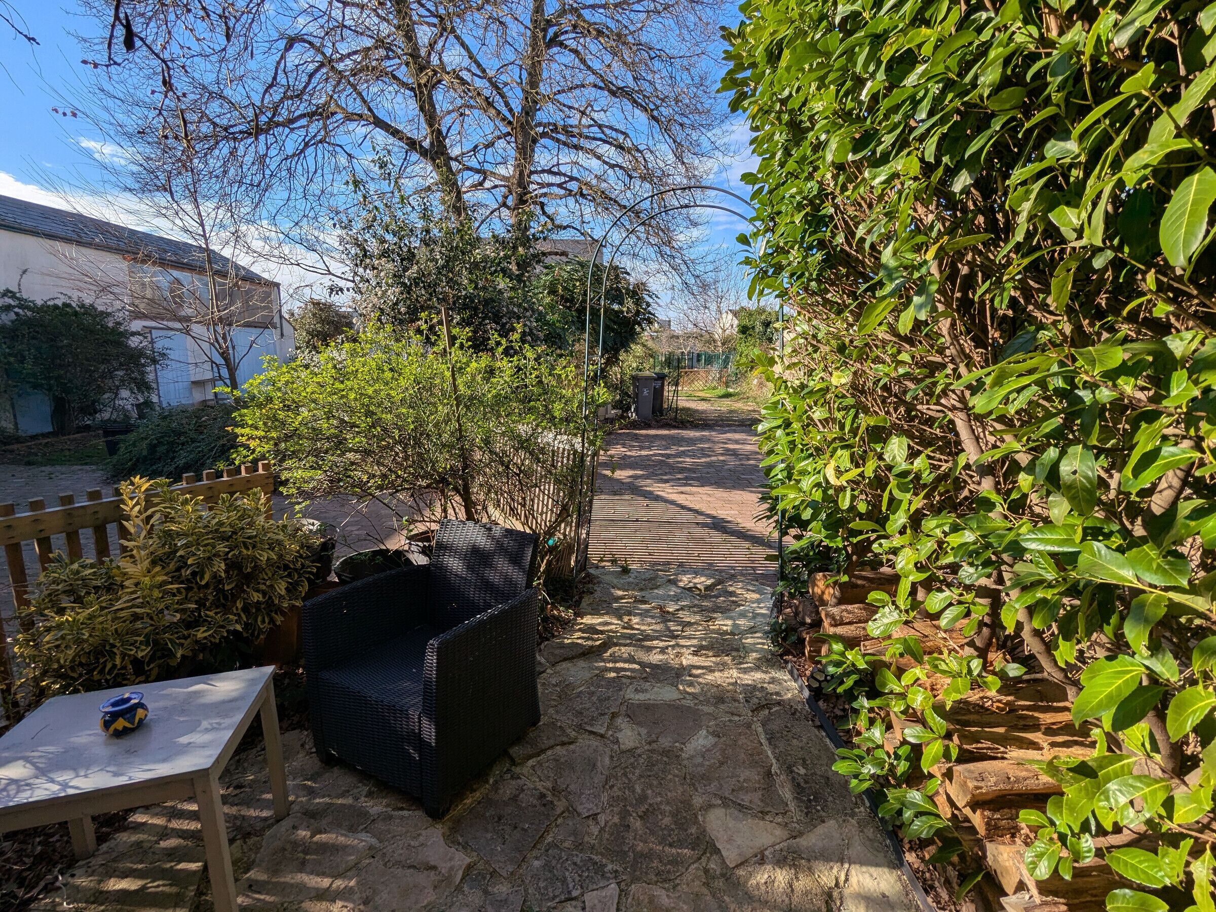 Un chemin de pierres qui traverse un jardin, avec un banc et des meubles en osier.