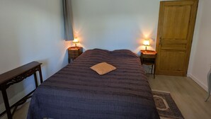 Een slaapkamer met een bed, twee nachtkastjes met lampen, een houten deur en een raam met gordijnen.
