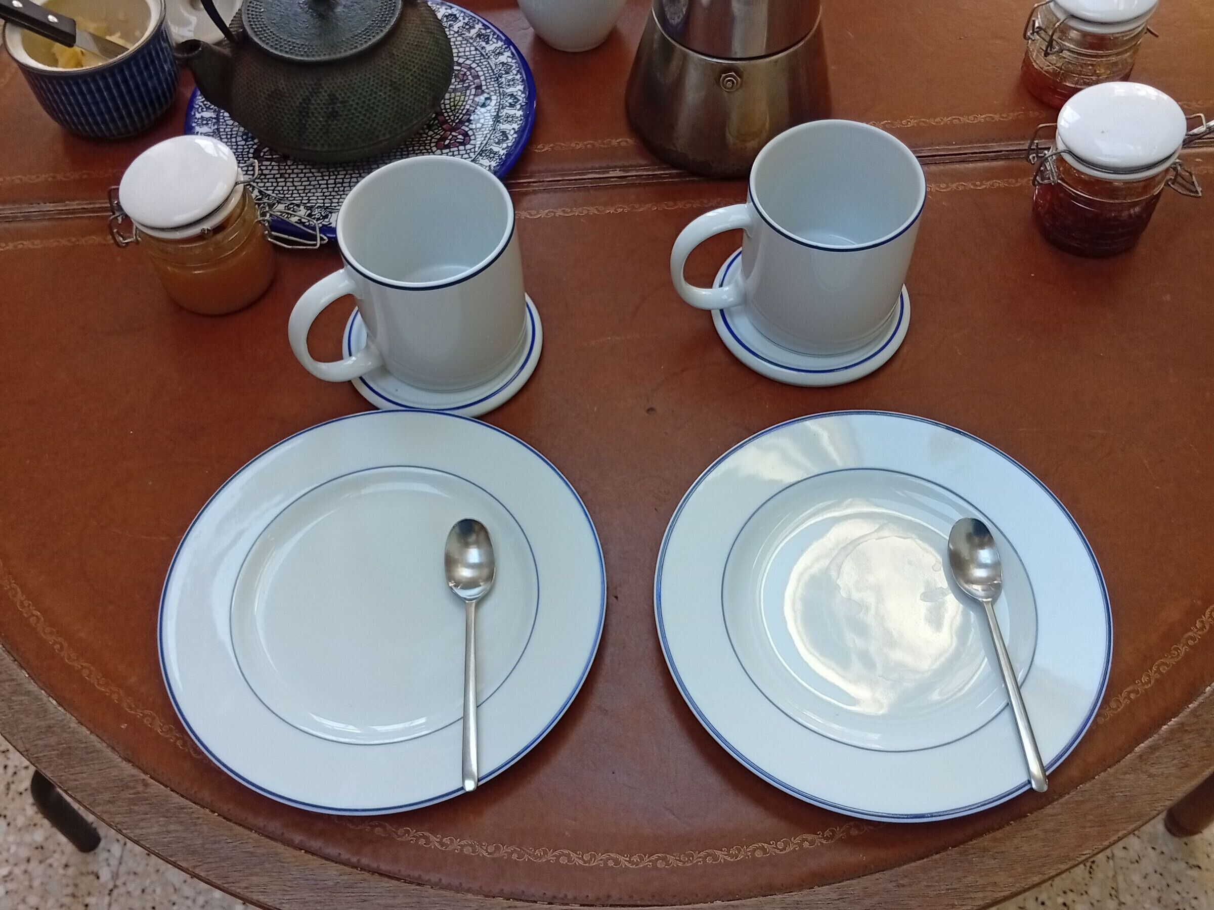 Une table avec deux assiettes blanches, chacune accompagnée d’une cuillère, et deux tasses blanches avec leurs soucoupes.
