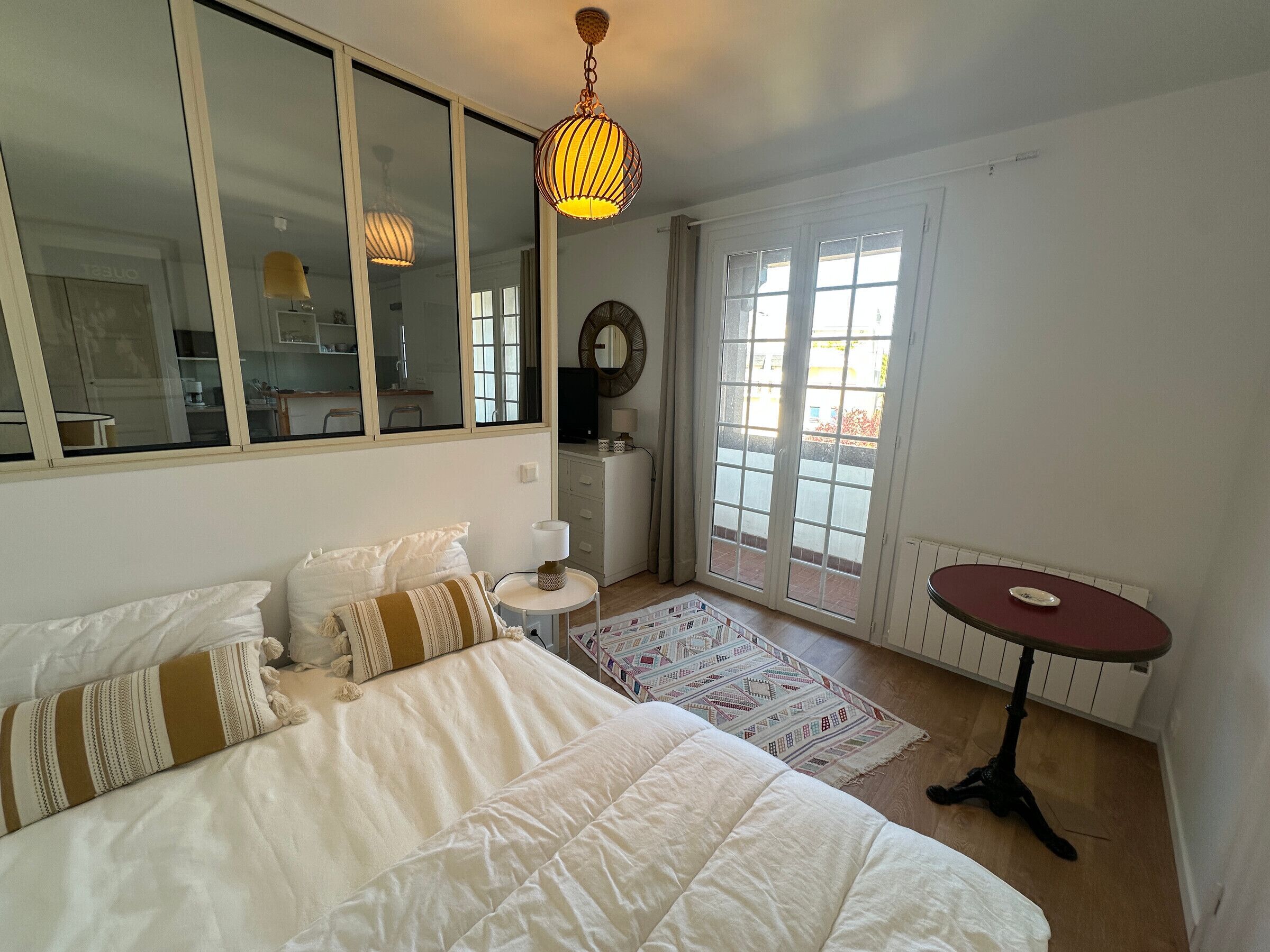 A bedroom with a bed, a desk, a chair, a mirror, and a window with a view.