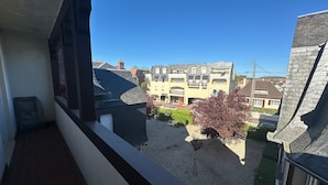 En balkong med utsikt över en byggnad med flera våningar och ett litet träd i förgrunden.