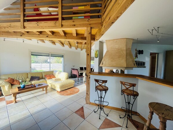 A spacious living area with a high ceiling, a sofa, a coffee table, and a kitchen area with a bar. - House near beach, pets welcome - 8 guests (Sarzeau)