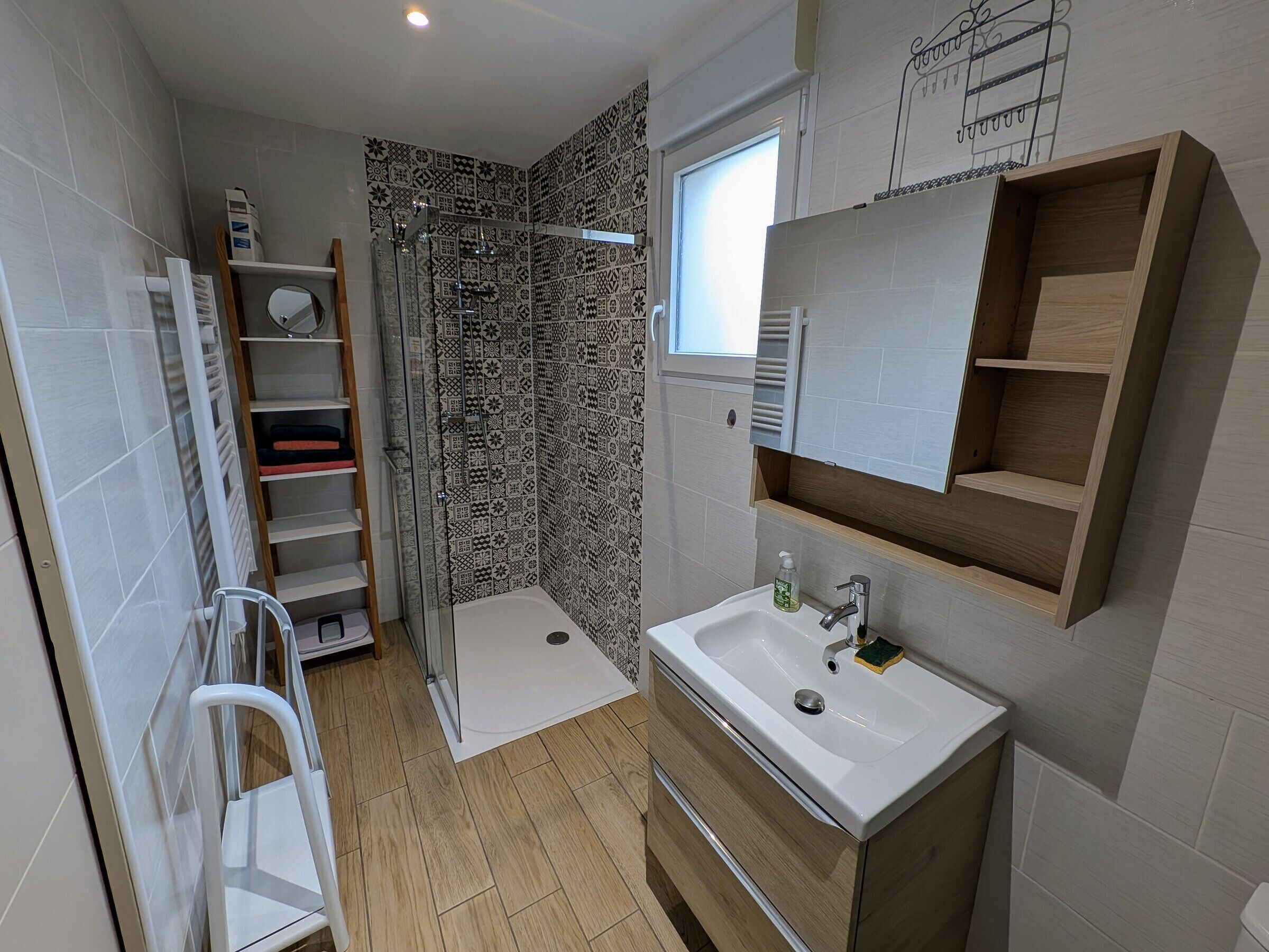 A modern bathroom with a shower, a sink, a mirror, and a storage shelf.