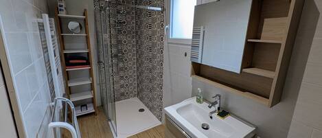 A modern bathroom with a shower, a sink, a mirror, and a storage shelf.