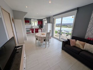 A modern living room with a sofa and a dining area with a table and chairs. - Peaceful cottage with shared pool, AC - 5 guests (Fretigney-et-Velloreille)