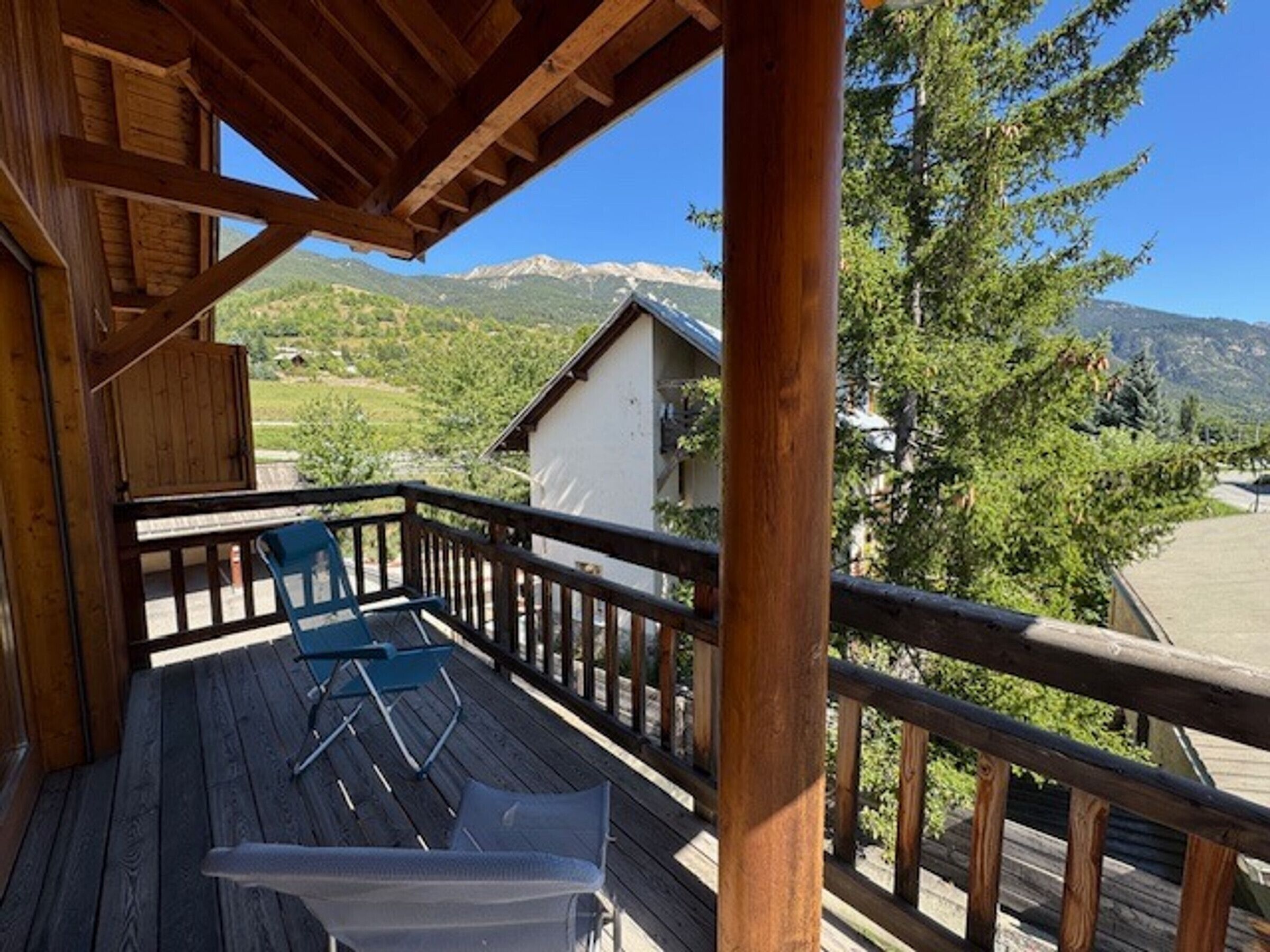 A wooden deck with a table and chairs, overlooking a mountainous landscape.